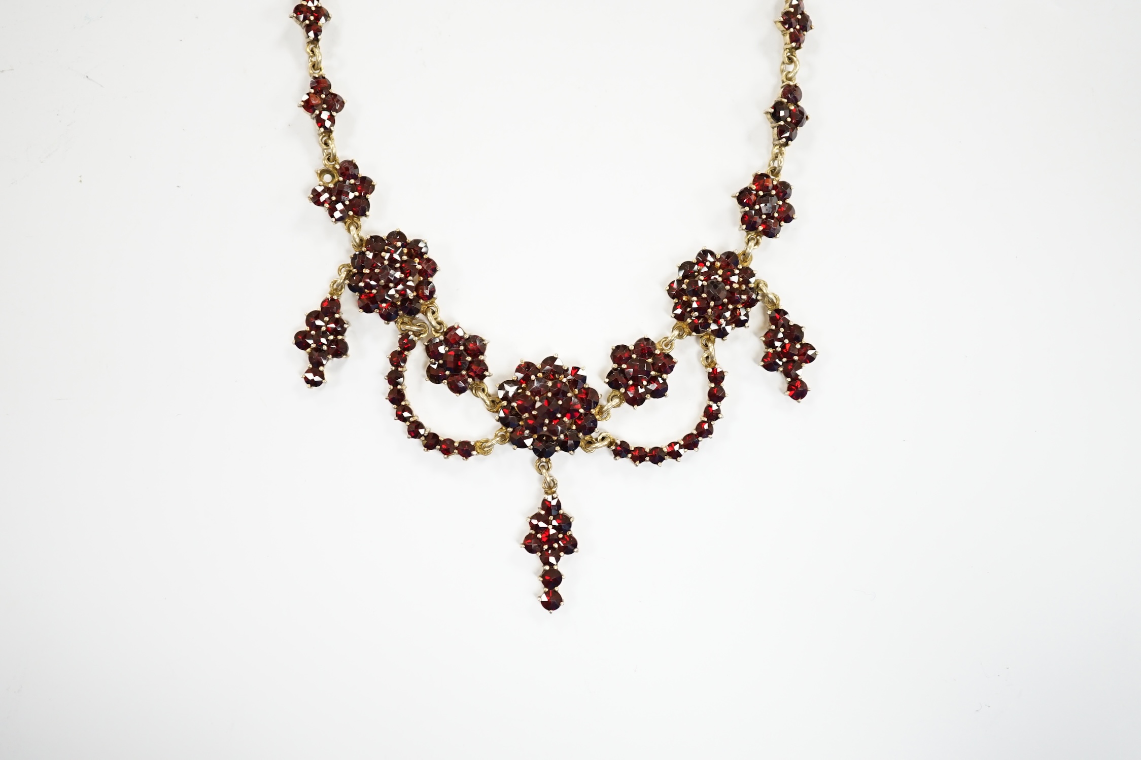 An early 20th century gilt sterling and garnet cluster set drop necklace, 45cm.